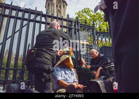 London, Großbritannien. 2.. September 2022. Die Polizei bedeckt einen Protestierenden, der am Zaun befestigt ist, mit Schutzmaterial, bevor er das Schloss durchschneidet. Die Demonstranten der Extinction Rebellion klebten sich im Parlament ein, während andere sich nach draußen sperrten und festklebten und eine Bürgerversammlung forderten. Kredit: Vuk Valcic/Alamy Live Nachrichten Stockfoto