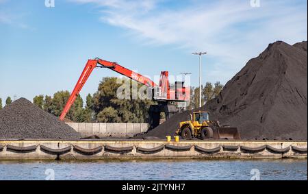 Ein Bild von einem Kran und einer Planierraupe neben großen Haufen Kies und Kohle in der Danziger Werft. Stockfoto