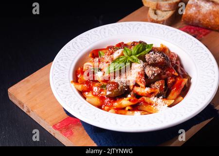 Lebensmittelkonzept hausgemachte sizilianische Bio-Pasta alla norma Penne mit Auberginen-Tomatensaucen auf Holzbrett auf schwarzem Hintergrund mit Kopierfläche Stockfoto