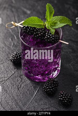 Erfrischender BlackBerry-Sommercocktail in Glas mit Eis und Minze auf schwarzem Hintergrund mit rohen Beeren. Makro Stockfoto