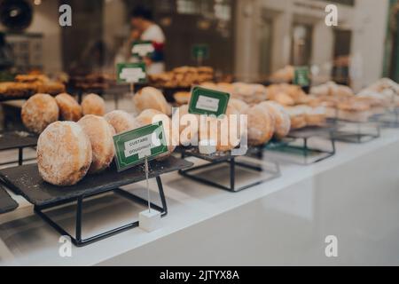 Nahaufnahme einer Vielzahl von Donuts auf einer Fensteransicht eines Cafés in London, Großbritannien. Selektiver Fokus. Stockfoto