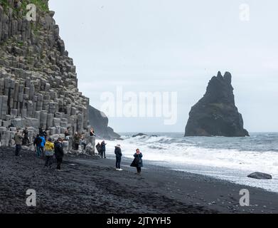 Touristen am Reynisfjara Strand, Klettern auf den Basaltsäulen und Ausweichen der Wellen, Island. Stockfoto