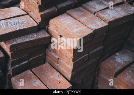 Stapel von neu hergestellten festen Ziegelsteinen aus Lehm (Backerde), die für die Landschaftsgestaltung und andere Gebäude- und Bauzwecke verwendet werden. Selektiver Fokus. Stockfoto