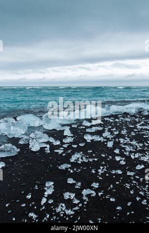 Eisbrocken brachen vom Gletscher ab, schweben ins Meer und waschen sich dann auf dem schwarzen Sand des Diamond Beach in Jökulsárlón, der Südküste Islands. Stockfoto