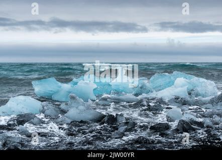 Eisbrocken brachen vom Gletscher ab, schweben ins Meer und waschen sich dann auf dem schwarzen Sand des Diamond Beach in Jökulsárlón, der Südküste Islands. Stockfoto