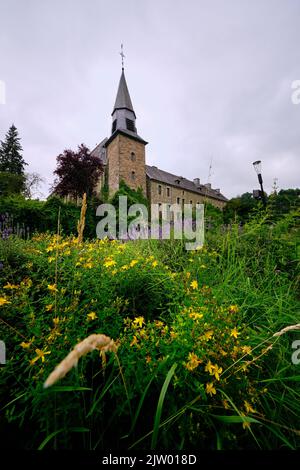 Blick auf die Katharinenkirche in Houffalize, Provinz Luxemburg, Belgien. Üppige Vegetation im Vordergrund Stockfoto