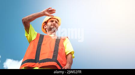 Ein Porträt eines Arbeiters steht mit Zuversicht in einem orangefarbenen Arbeitsanzug und Schutzhelm gegen den Himmel. Intelligentes Arbeitskonzept für Industriearbeiter. Stockfoto