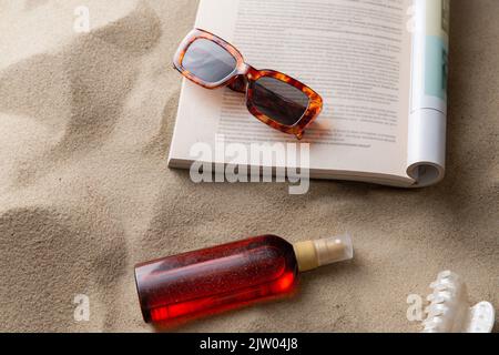 Magazin, Sonnenbrillen und Sonnencreme auf Strandsand Stockfoto