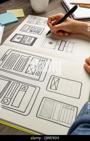 UI Designer skizziert die Benutzeroberfläche einer Webanwendung für ein Mobiltelefon. Ein Entwickler erstellt einen Prototyp für ein Smartphone. Stockfoto