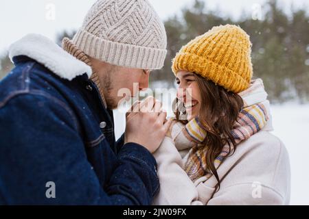 Glücklicher Mann, der die Hände der Frau im Winterpark wärmte Stockfoto