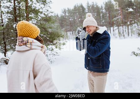 Glücklicher Mann fotografiert Frau im Winterwald Stockfoto
