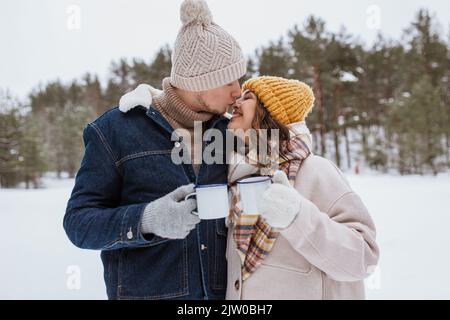 Glückliches Paar mit Teetassen im verschneiten Winterpark Stockfoto