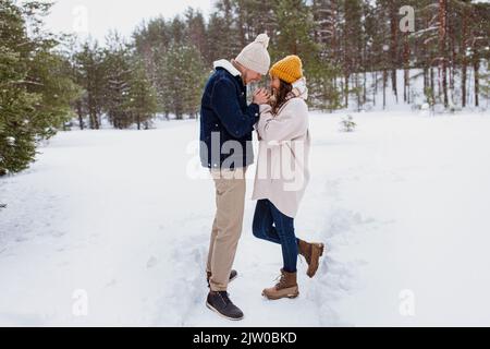 Glücklicher Mann, der die Hände der Frau im Winterpark wärmte Stockfoto