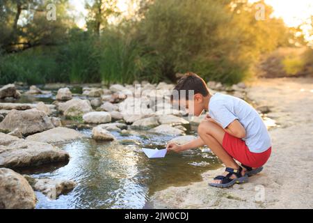 Im Sommer spielt das Kind mit einem Papierboot im Flusswasser Stockfoto