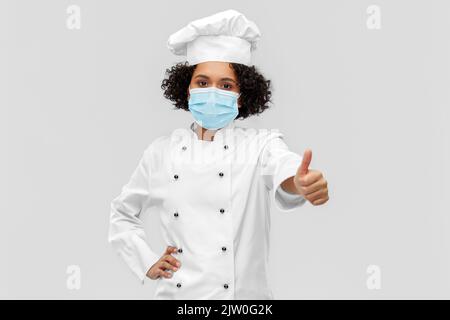 Weibliche Köchin in medizinischer Maske zeigt Daumen nach oben Stockfoto