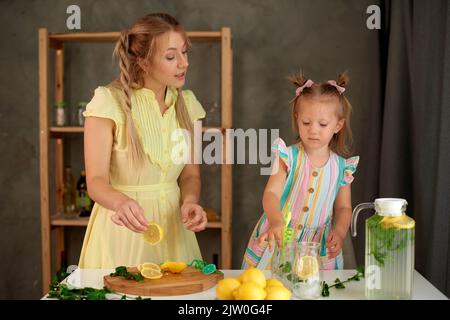 Kleines Mädchen hilft Mama in der Küche, Limonade für Erfrischungsgetränke zuzubereiten Stockfoto