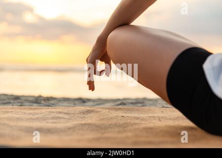 Frau, die am Strand in Lotuspose meditiert Stockfoto