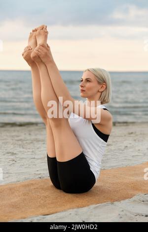 Frau beim Yoga-Boot am Strand Stockfoto