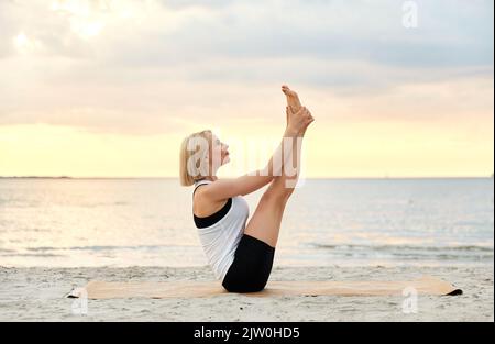 Frau beim Yoga-Boot am Strand Stockfoto