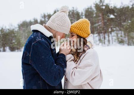 Glücklicher Mann, der die Hände der Frau im Winterpark wärmte Stockfoto