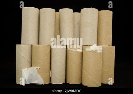Eine Reihe leerer Toilettenpapierrollen, die in zwei Reihen vor einem schwarzen Hintergrund gestapelt wurden Stockfoto