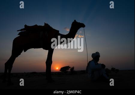 Silhouette des alten Kamels und seines Kamels an den Sanddünen der Thar-Wüste, Rajasthan, Indien. Wolke mit untergehenden Sonne, Himmel im Hintergrund. Kameraleuten machen Stockfoto