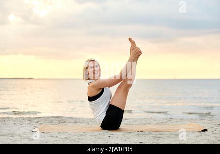 Frau beim Yoga-Boot am Strand Stockfoto