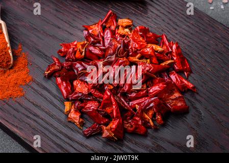 Stücke von getrocknetem Paprika, Vorbereitung von Pulvergewürz für verschiedene Gerichte, vor einem dunklen Betongrund Stockfoto
