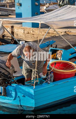 griechischer Fischer, der im Hafen von chania auf kreta auf dem Boot arbeitet, Fischer, der Netze repariert, Fischer in griechenland, der das Boot vor der nächsten Reise führt, Fisch. Stockfoto