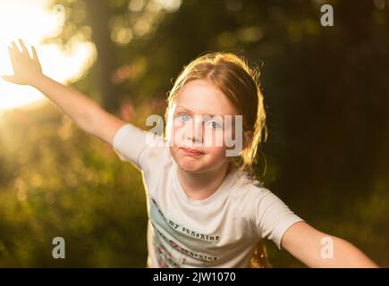 Young Girl blickt mit einer Mischung aus Blitzaufnahmen in die Kamera und stellt sich bei Sonnenuntergang in einer auswappnen Pose. Stockfoto