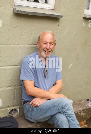 Der alte Kaukasusmann sitzt und lächelt für die Kamera. Stockfoto