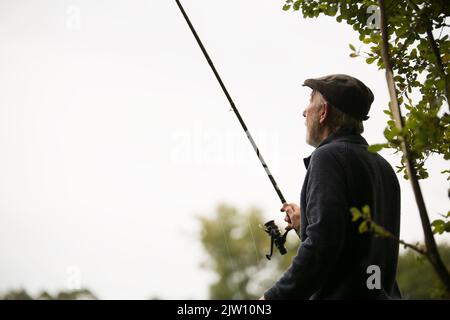 Alter Mann mit einer Angelrute, die draußen nach außen schaute. Stockfoto