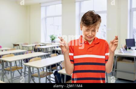 Schüler Junge mit gekreuzten Daumen in der Schule Stockfoto