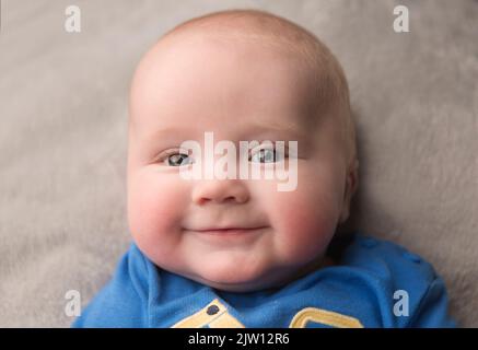 Kaukasischer Junge, lächelnd in die Kamera, während er sich hinlegt, benutzte Studiolicht. Stockfoto