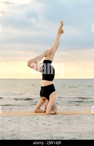 Frau macht Yoga Kopfstand am Strand Stockfoto