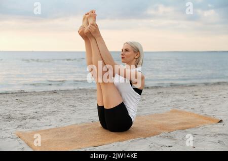 Frau beim Yoga-Boot am Strand Stockfoto