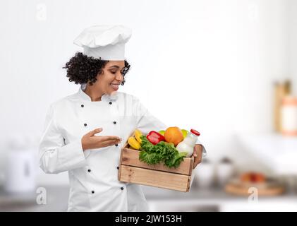 Weibliche Köchin mit Essen in Holzkiste in der Küche Stockfoto