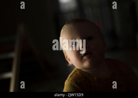 Kleinkind männlich Blick in die Kamera, während auf dem Boden spielen, Studiolicht in einem dunklen Raum verwendet. Stockfoto