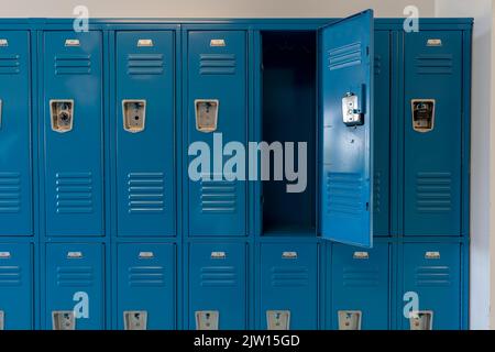 Schließfächer aus blauem Metall entlang eines unscheinbaren Flurs in einer typischen US High School. Keine identifizierbaren Informationen enthalten und niemand in der Halle. Stockfoto