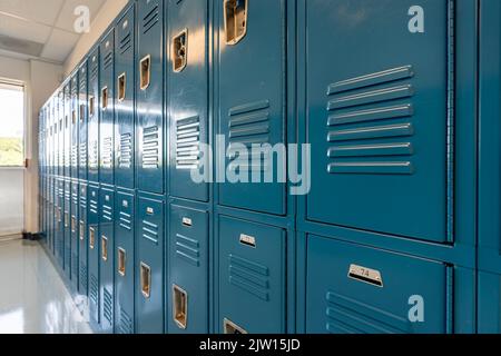 Schließfächer aus blauem Metall entlang eines unscheinbaren Flurs in einer typischen US High School. Keine identifizierbaren Informationen enthalten und niemand in der Halle. Stockfoto