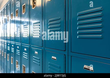 Schließfächer aus blauem Metall entlang eines unscheinbaren Flurs in einer typischen US High School. Keine identifizierbaren Informationen enthalten und niemand in der Halle. Stockfoto