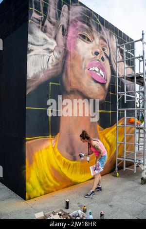 Veranstaltung „Southend City Jam“. Straßenkünstler zeigen ihre Fähigkeiten an 60 Orten im Stadtzentrum. Weibliche Künstlerin Spray Malerei schwarze Figur Stockfoto