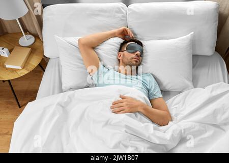 Mann in Augenmaske schläft im Bett zu Hause Stockfoto