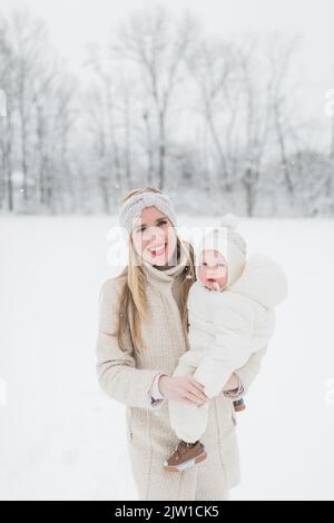 Blonde, kaukasische Mutter hält gebündeltes Baby im Schnee. Stockfoto