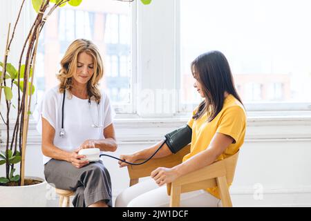 Reifer Arzt, der den Blutdruck einer Patientin in der Klinik überprüft Stockfoto