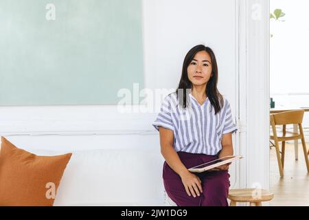 Porträt einer selbstbewussten Geschäftsfrau mit digitalem Tablet, die im kreativen Büro auf dem Sofa sitzt Stockfoto