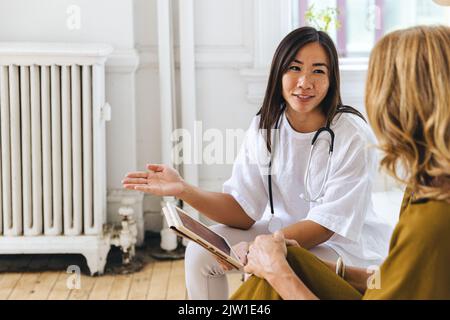 Lächelnde Ärztin, die im Krankenhaus mit einer Patientin über elektronische Krankenakten diskutiert Stockfoto