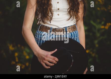 Teen Mädchen hält Cowboy Hut durch Gürtelschnalle Stockfoto