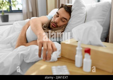 Kranker Mann liegt im Bett und nimmt Gewebe vom Tisch Stockfoto