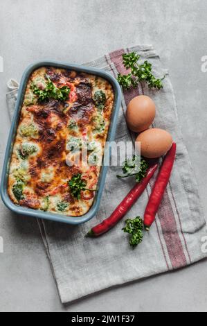 Auflaufform, rohe Eier, Chili und lockige Petersilie. Stockfoto